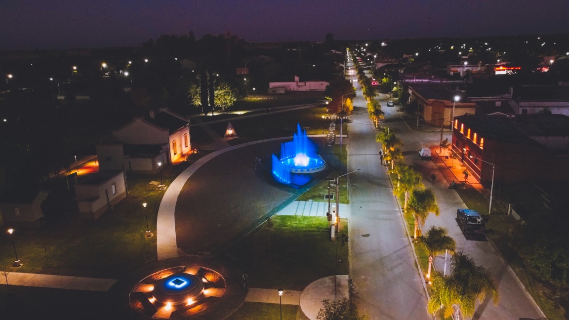 Vista aérea nocturna del centro de Winifreda, con la avenida principal y una fuente iluminada