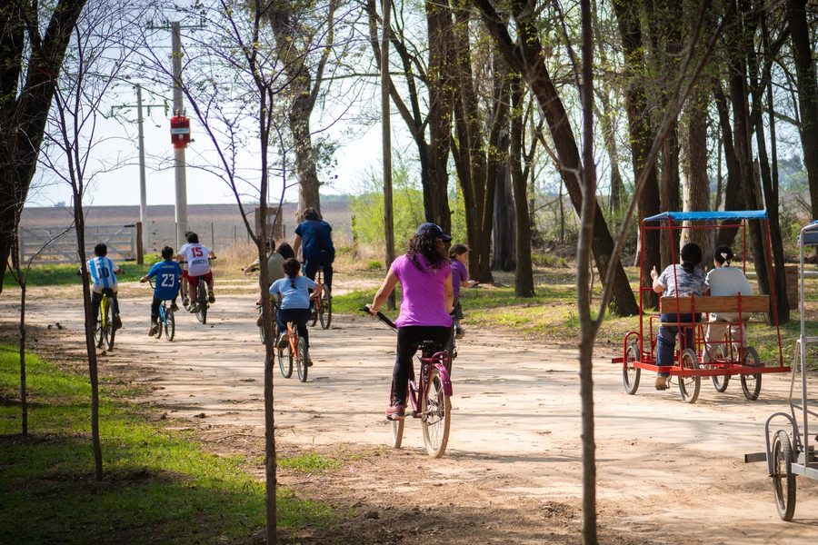 Chicos en bicicleta por los caminos internos del Vivero Municipal, con un carro familiar de paseo detrás
