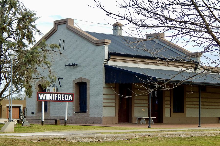 La antigua estación de ferrocarril de Winifreda de día, con su andén, la galería y el cartel ferroviario original