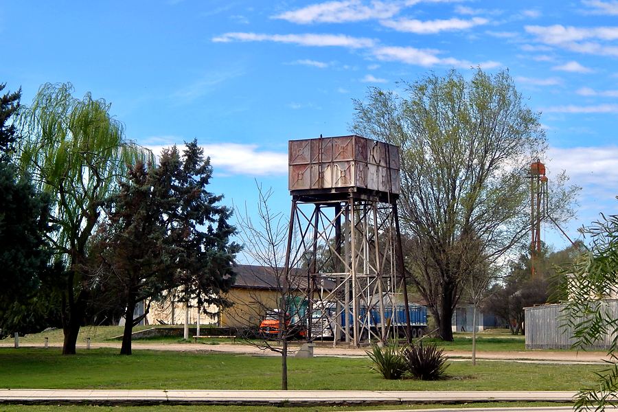 El antiguo tanque de agua del ferrocarril sobre su estructura de hierro, entre los sauces del paseo